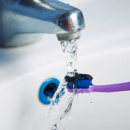 Toothbrush being rinsed under running water in sink