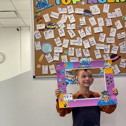 a child standing in front of a corkboard and smiling at Tooth Clues