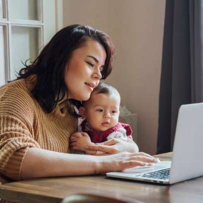 Woman typing on laptop with baby sitting in her lap