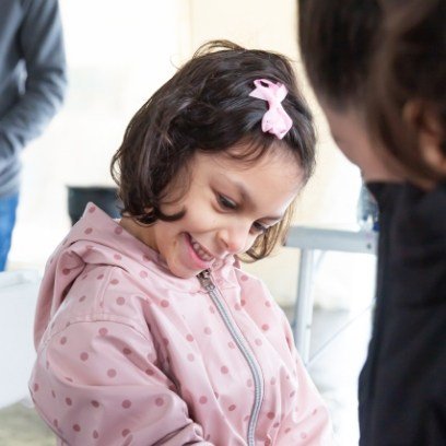 Young girl in pink jacket smiling while looking down at floor