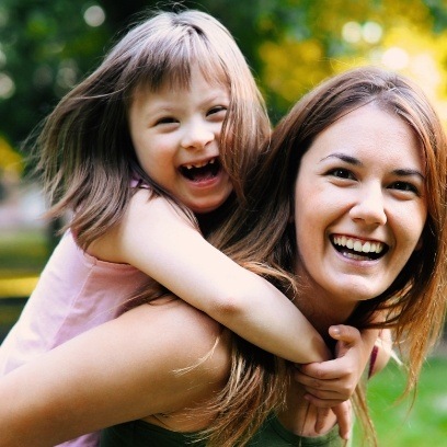 Mother giving young daughter with special needs a piggyback ride outdoors