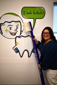 a tooth clues team member holding a huge toothbrush next to a wall mural of a smiling molar